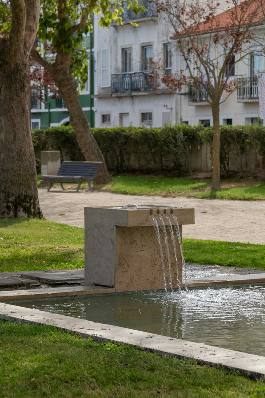 A water fountain in a park with a bench in the background