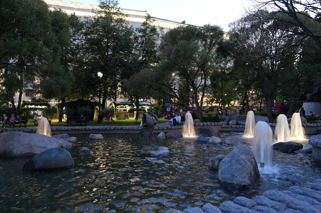 A fountain in a park glows at dusk.