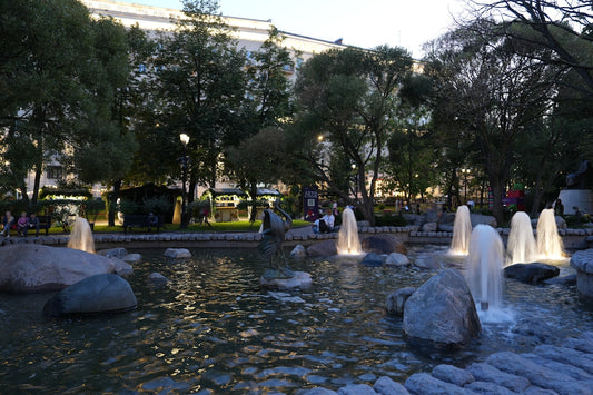 A fountain in a park glows at dusk.