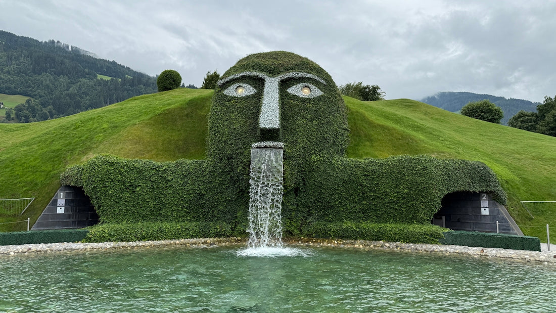 A large green sculpture spills water into a pond.